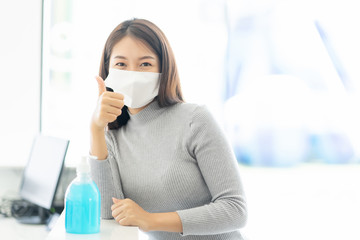 Fototapeta na wymiar Woman wearing face mask protective for spreading of disease virus SARS-CoV-2 and show hand thumb up after clean alcohol in office for protection bacteria and virus, Covid-19 Coronavirus concept