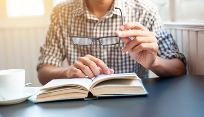 The young man with vision problems is picking up his glasses and reading a book.