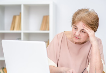 Sad elderly woman looks at laptop in the office