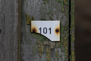 broken plastic sign with a number 101 on a wooden door with peeling paint 