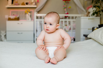 Cute fat toddler girl smiles in diapers sitting on bed at home