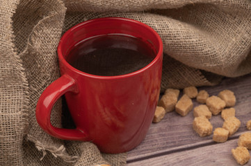 A red ceramic mug of tea and chunks of brown cane sugar. Close up.