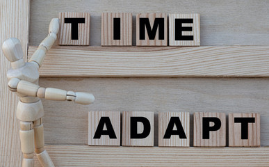 TIME , ADAPT words are written on the board. Nearby is a wooden man. Business concept.