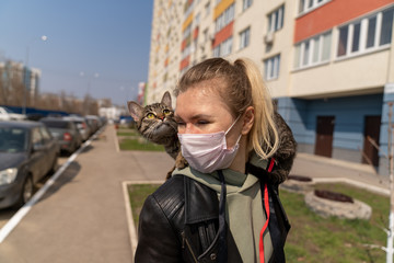 Obraz premium a girl in a medical mask is walking with a kitten on her shoulder