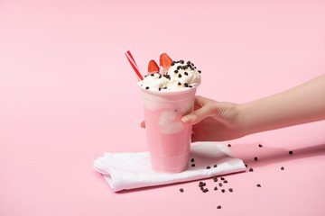 Cropped view of female hand with disposable cup of milkshake with chocolate morsels and strawberry...