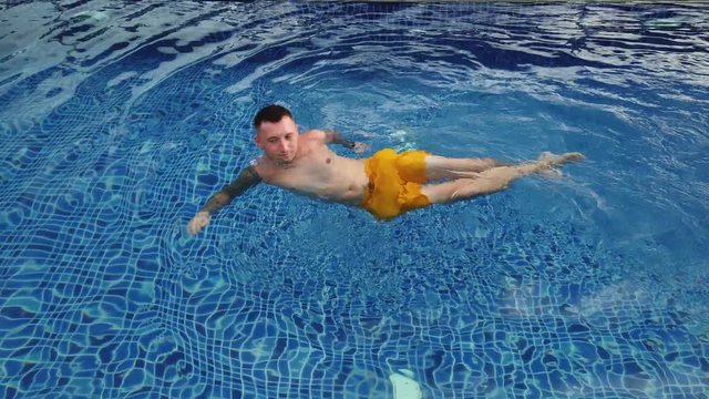 Tattooed man swims in blue pool