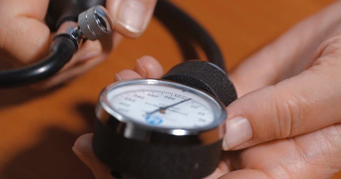 Close-up detail shot of hands of an elderly woman measuring  blood pressure using  a mechanical tonometer on a brown wooden table at home. 4k 50fps slow motion