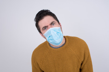 Expressive facial expressions. Shocked stupefied male wearing medical face mask keeps jaw dropped, feels stunned from what he sees aside on blank gray Wall