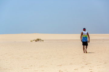 Fototapeta na wymiar A young handsome man walking on the sand of the dunes in a beach of Fuerteventura