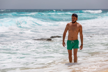 Fototapeta na wymiar A young man with green swimming trunks walking through the water in a beach of Fuerteventura, Canary Islands, Spain