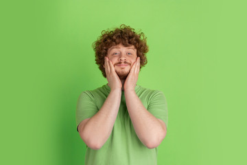 Shocked, astonished, wondered. Caucasian young man's monochrome portrait on green studio...