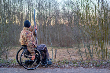 man on wheelchair and camouflage, hunter waiting for woodcock arrival in spring evening forest,...