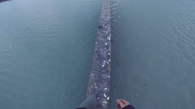 Man walks on Seawall. Wearing white shoes he looks down with water from the still lake on both sides. Walking and balancing on the metal Sea Wall, he traverses with courage to the end. 4K capture.