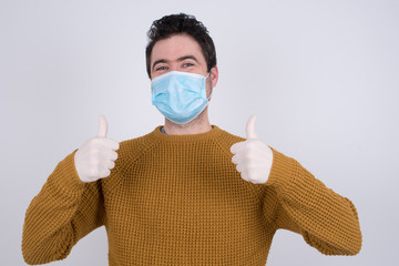 Closeup of young optimistic male wearing medical face mask showing thumbs up with positive emotions of content and happiness. Copyspace, concept of satisfaction with quality and recommendation.