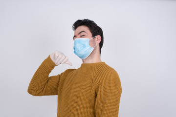 Closeup of cheerful handsome European man wearing medical face mask looks joyful, satisfied and confident, points at himself with thumb, isolated over gray studio background.