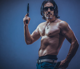 sexy muscular body model portrait of a young man holding a gun in his hands,black glasses on the eyes