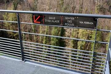 Obraz premium Panneau indiquant la salle d'escalade, le sentier des Poules et la Via Ferrata sur une barrière en mètal. Saint-Gervais-les-Bains. Haute-Savoie. France.