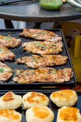 Delicious chicken steaks and fried bread buns on a grill.
