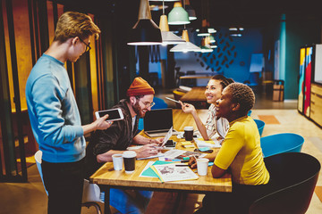 Cheerful prosperous business partners enjoying productive cooperation sitting at table in coworking space,successful diverse team of designers making research discussing ideas in friendly atmosphere