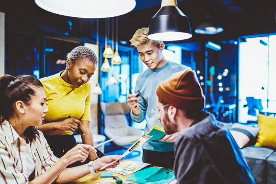 Skilled Male And Female It Professionals Sitting Together At Meeting Table Analyzing Revenue And Reports For Startup, Smart Diverse Team Of Colleagues Communicating And Researching On Consultancy