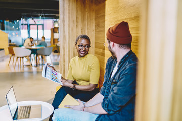 Cheerful male and female employees having friendly conversation sitting in coworking space together...