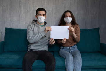 Quatantine concept: young caucasian couple in medical masks holding mockup