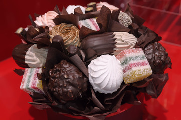 Holiday gift bouquet with sweets on red background. Delicious bouquet of marshmallows, souffles, chocolate, candy and other sweets.