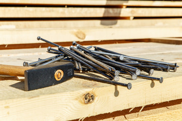 Iron nails and a hammer on a wooden background. Long, metal, carpenter's nails and a mallet lie on a bar for construction. Side view close-up.
