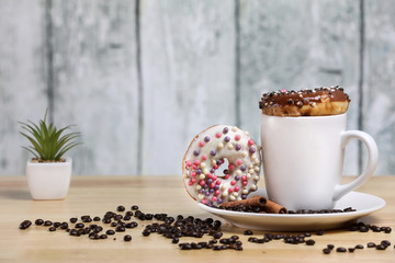 White coffee cup on a wooden table with chocolate and white chocolate donuts . Morning espresso. Morning cappuccino mug. 