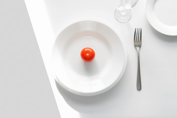 Table setting example. white plates on a white background in the light of the sun. Tomato on a...