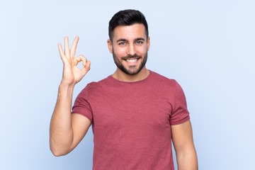 Young handsome man with beard over isolated blue background showing ok sign with fingers