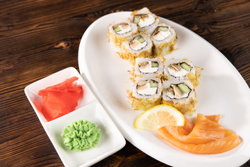 Rolls with salmon, cheese and avocado on oval plate. Wasabi and ginger on square plates on dark wooden table