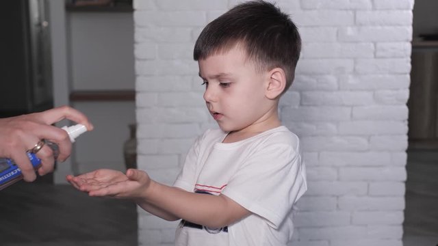 A mother  splashes antiseptic on the child's hands ah home. The concept of protection against coronavirus infections covid-19
