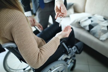 Close-up of male businessman giving keys from new house to disabled woman. Female sitting in wheelchair. Moving day into apartment. Handicapped and real estate concept