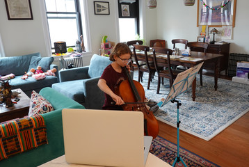 New York, USA. 2020. Schoolgirl learning to play a Cello using a laptop  to watch and listen her...