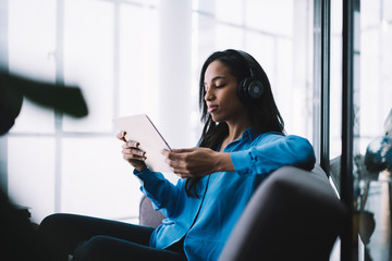Young African American woman in headset sitting on couch and looking at tablet screen