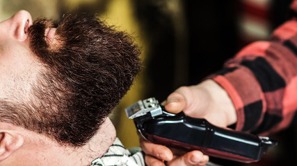 Brutal bearded guy getting beard haircut by hairdresser at barbershop, close up. Getting perfect shape.