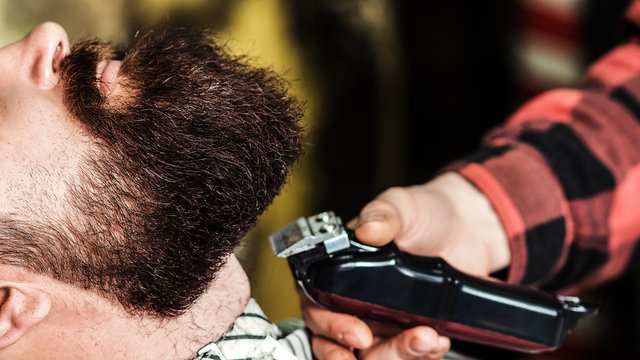 Brutal bearded guy getting beard haircut by hairdresser at barbershop, close up. Getting perfect shape.