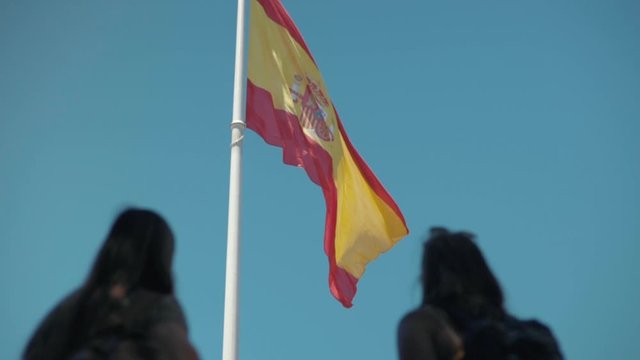 Two Spanish woman looking at the Spanish flag waving in the wind
