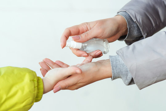 Family applying hand sanitizer to clean and disinfect hands. Woman applying alcohol spray against coronavirus. Mother and son using sanitizer spray for hands outdoors.