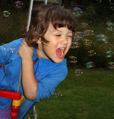 Small girl swinging on seesaw and playing with soap bubbles 