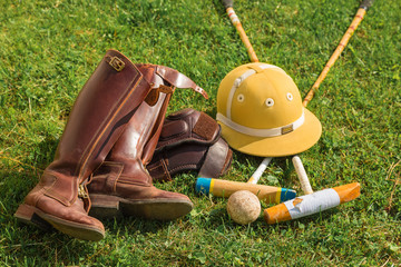 Equipment for a player in horse polo lies on a green lawn. Leather riding boots, protective helmet...