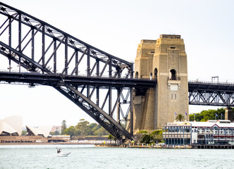 Fototapeta premium The pillars of the famous and beautiful Sydney Harbor Bridge and in the background is the Sydney Opera House, modern architecture and beautiful scenery of nature and human art