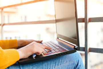 Fototapeta premium Woman working on a laptop on balcony, close up. Freelancer, remote work. Coronavirus quarantine.