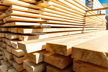 Stack of new wooden studs at the lumber yard. Timber on the construction site to dry. Background of sawed and processed wood of coniferous breeds.