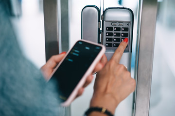 Cropped image of female entering secret key code for getting access and passing building using application on mobile phone, woman pressing buttons on control panel for disarming smart home system
