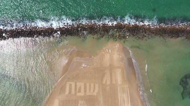 Happy Holiday in Hebrew letters written in Sand on a beach, Aerial view.
