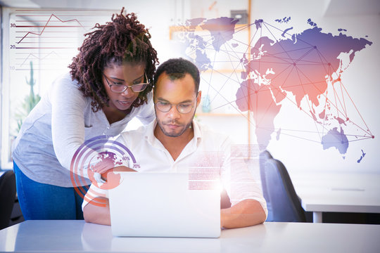 Professional helping with report and virtual statistic graphics. Business man and woman in casual sitting and standing at workplace, using laptop, pointing at screen. Mentorship concept