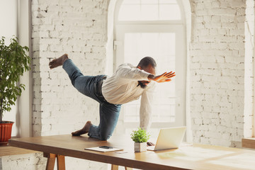 Young african-american man doing yoga at home while being quarantine and freelance online working....