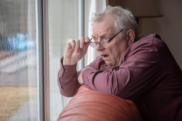 Fototapeta Shocked senior man looking out of window, nosy neighbor obraz